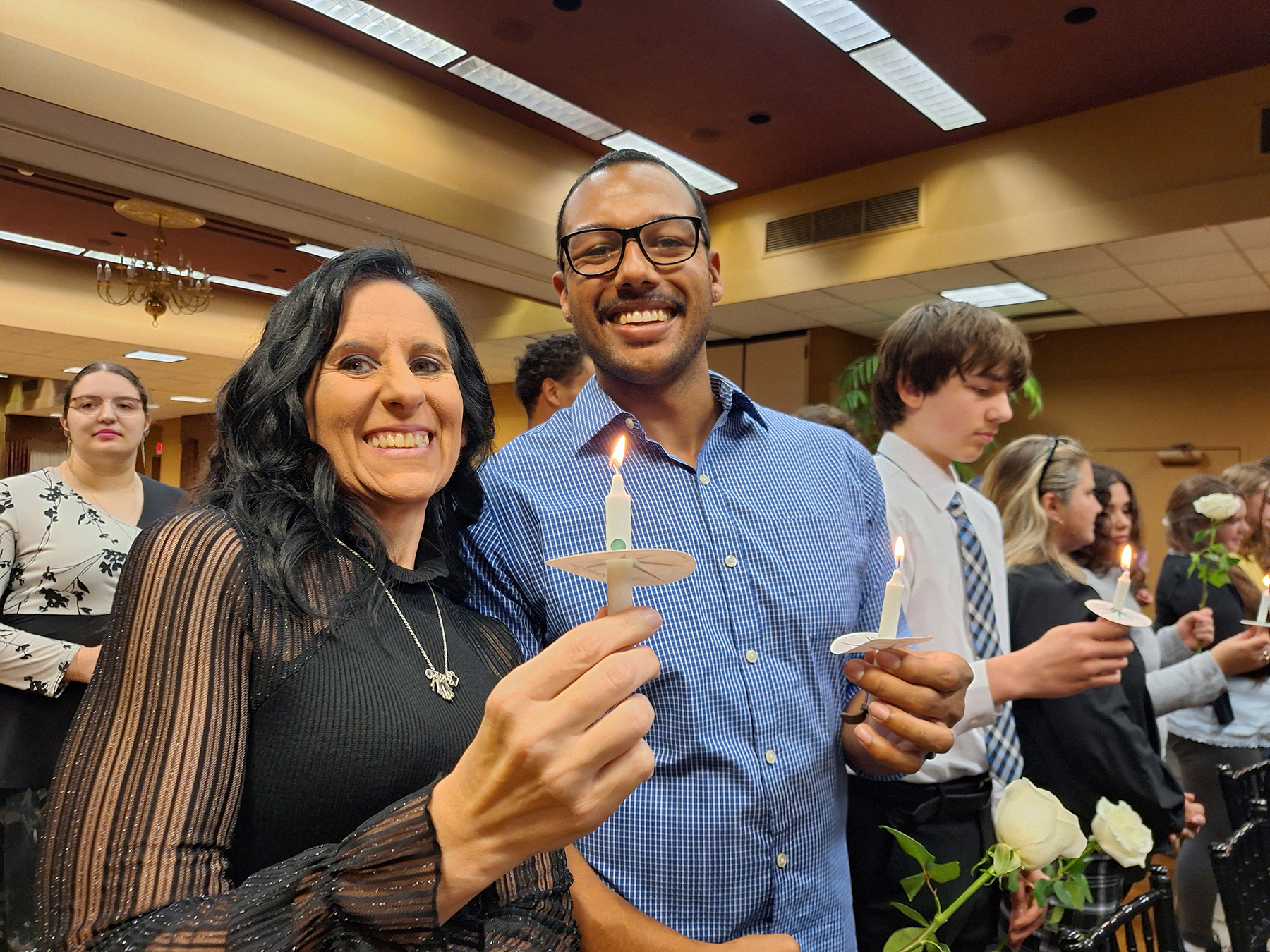 Students standing up holding white candles, smiling