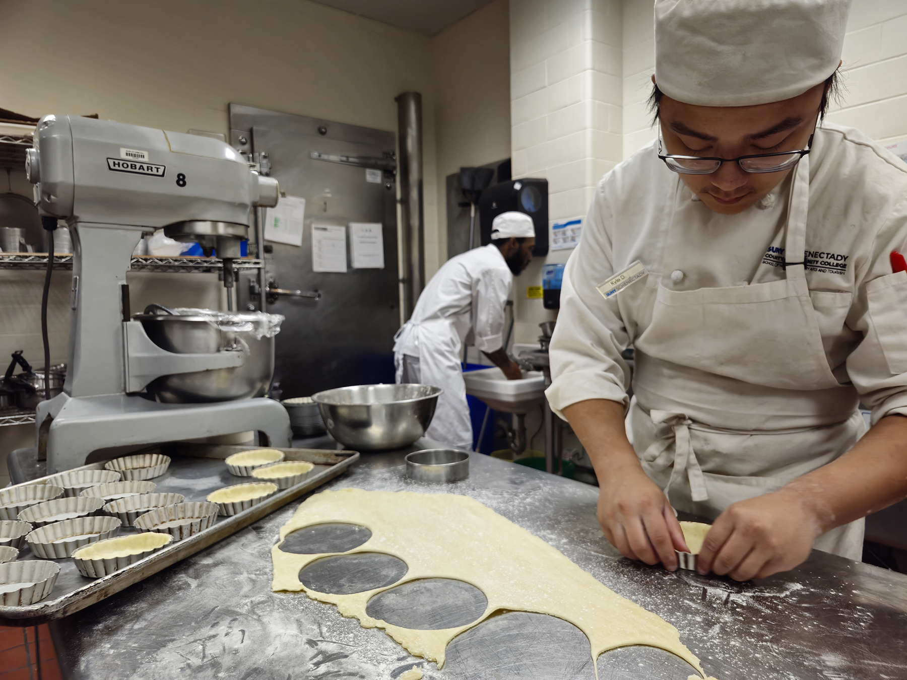Student cutting dough in kitchen