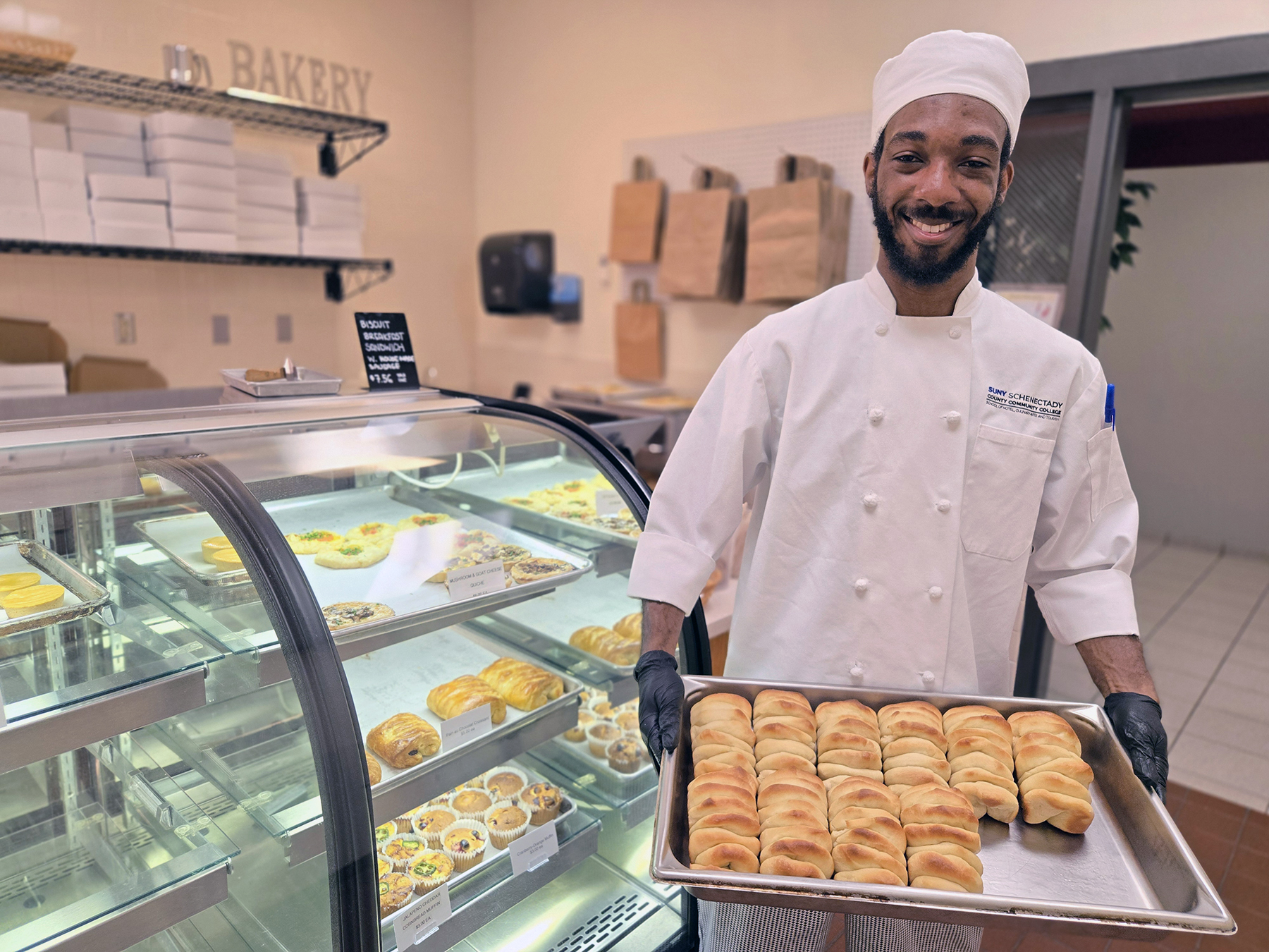 Student holding tray of pull-apart bread inside bakery