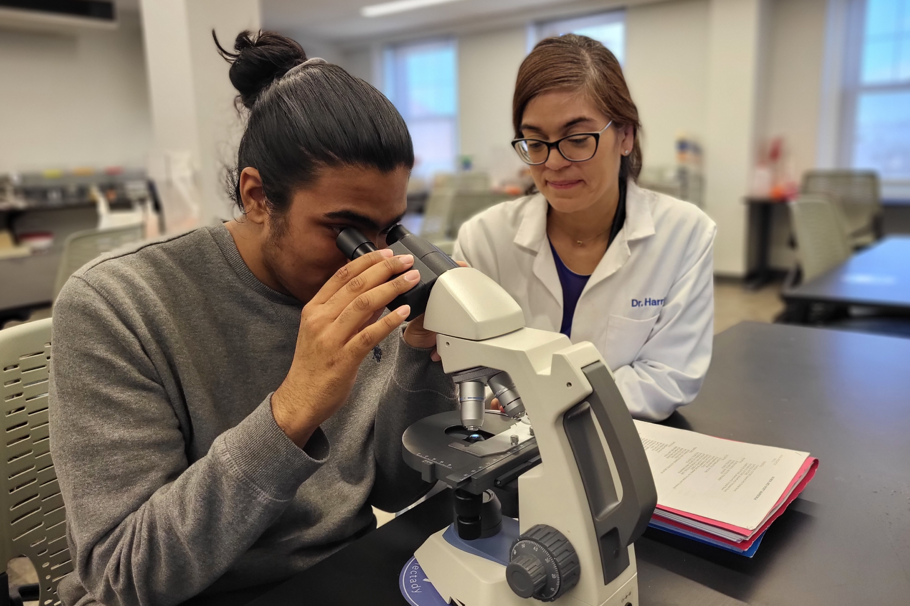 Parmesh Thakoordial looking at microscrope and Dr. Lorena Harris, seated at table in Biotech Lab