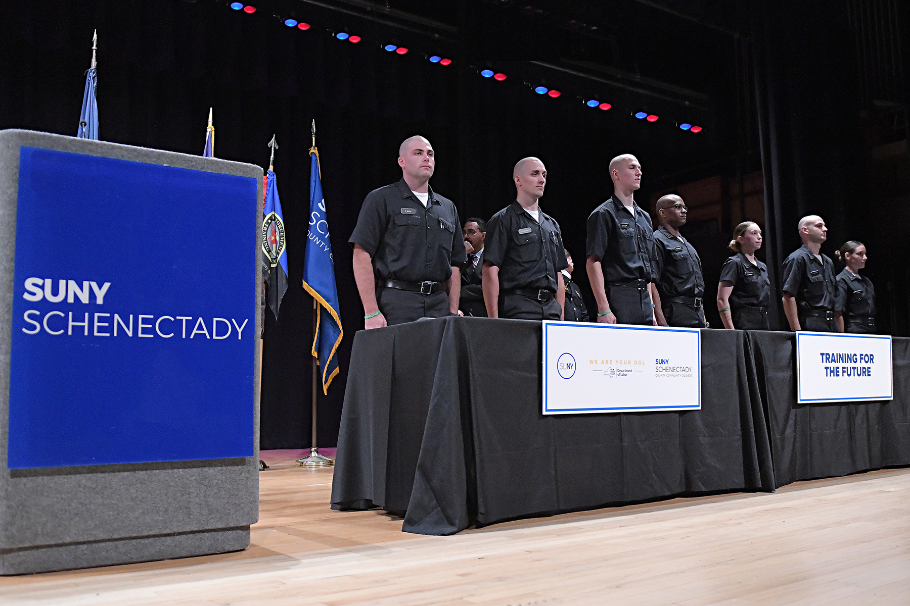 Police recruits lined up, standing on stage.