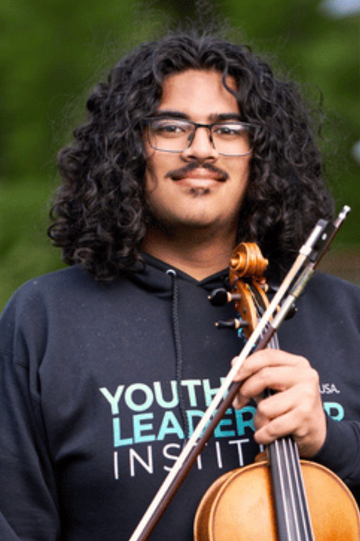 Randy Thakoordial, holding violin, smiling