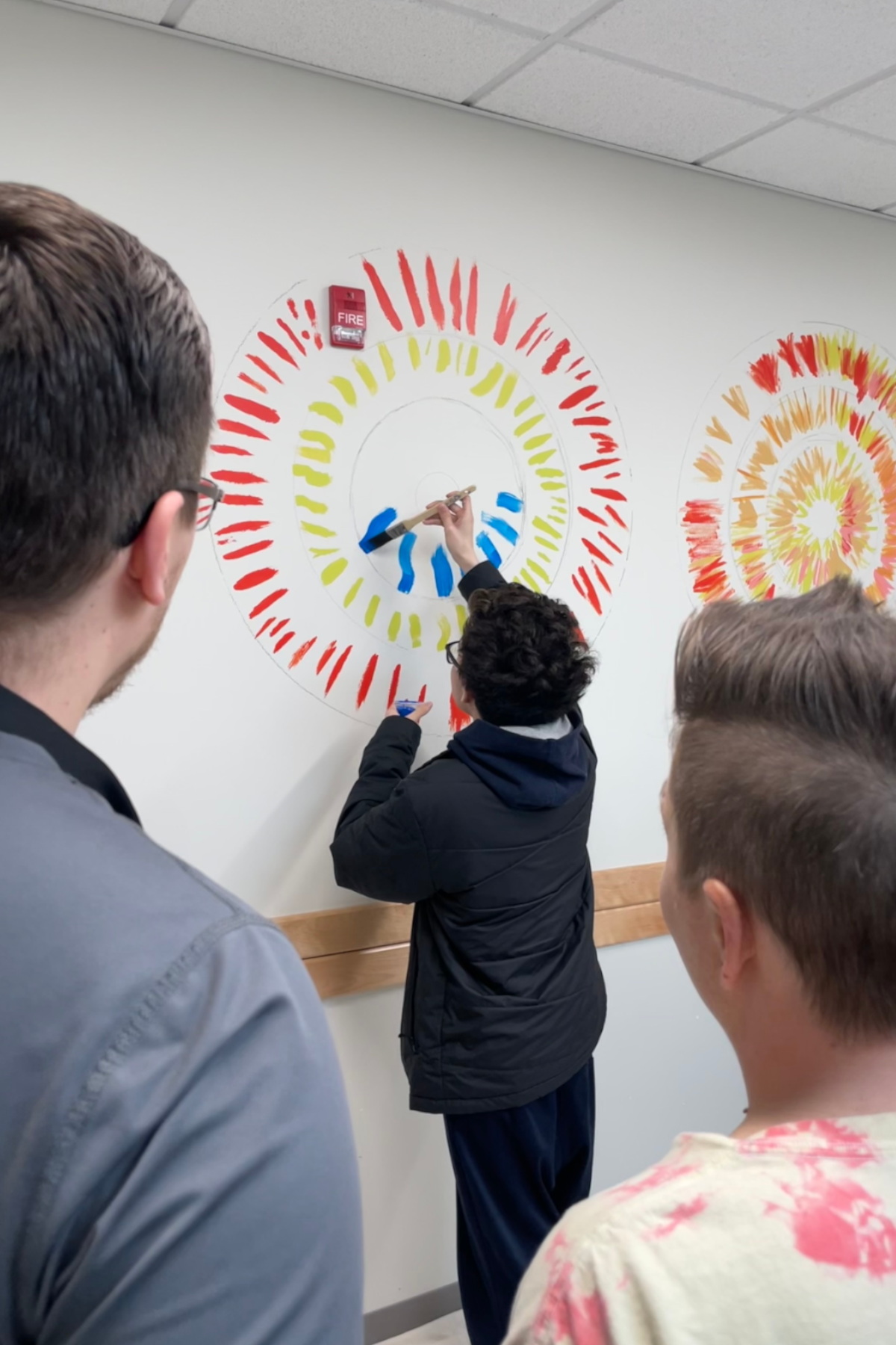 Student standing, painting artwork on wall 