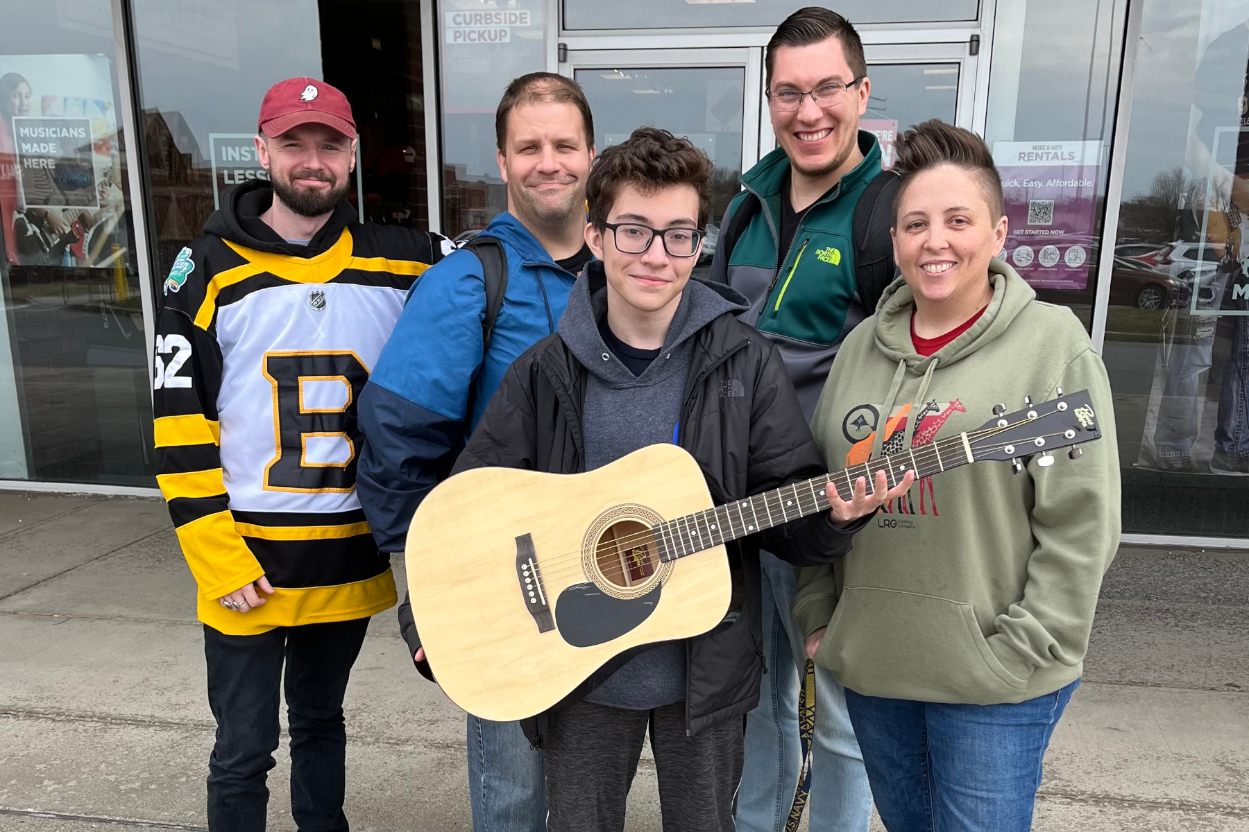 Students in front of music store, smiling, holding guitar