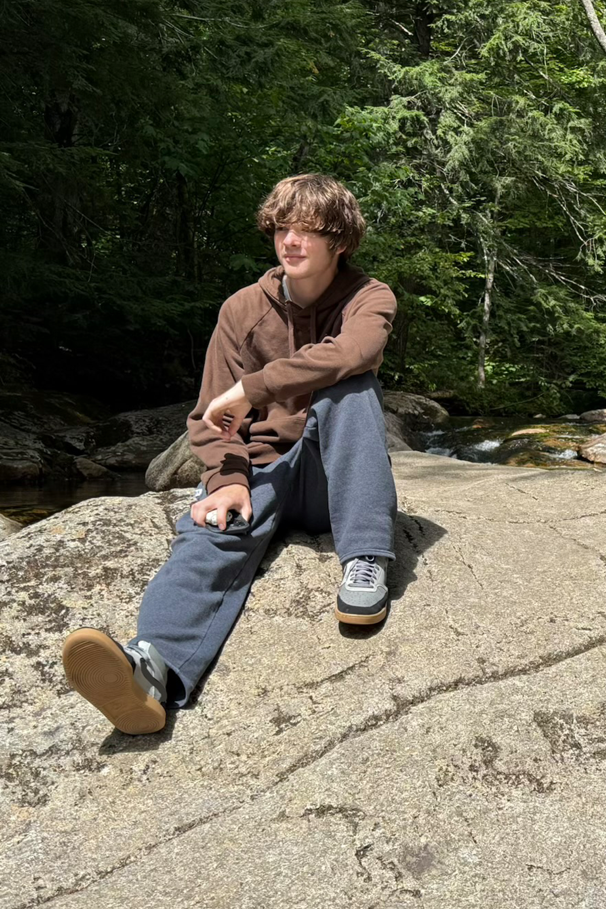 River Henriksen, outside, sitting on rocks near river