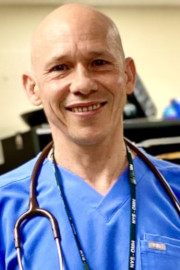 Ron Dayter in blue scrubs with a stethoscope around his neck.
