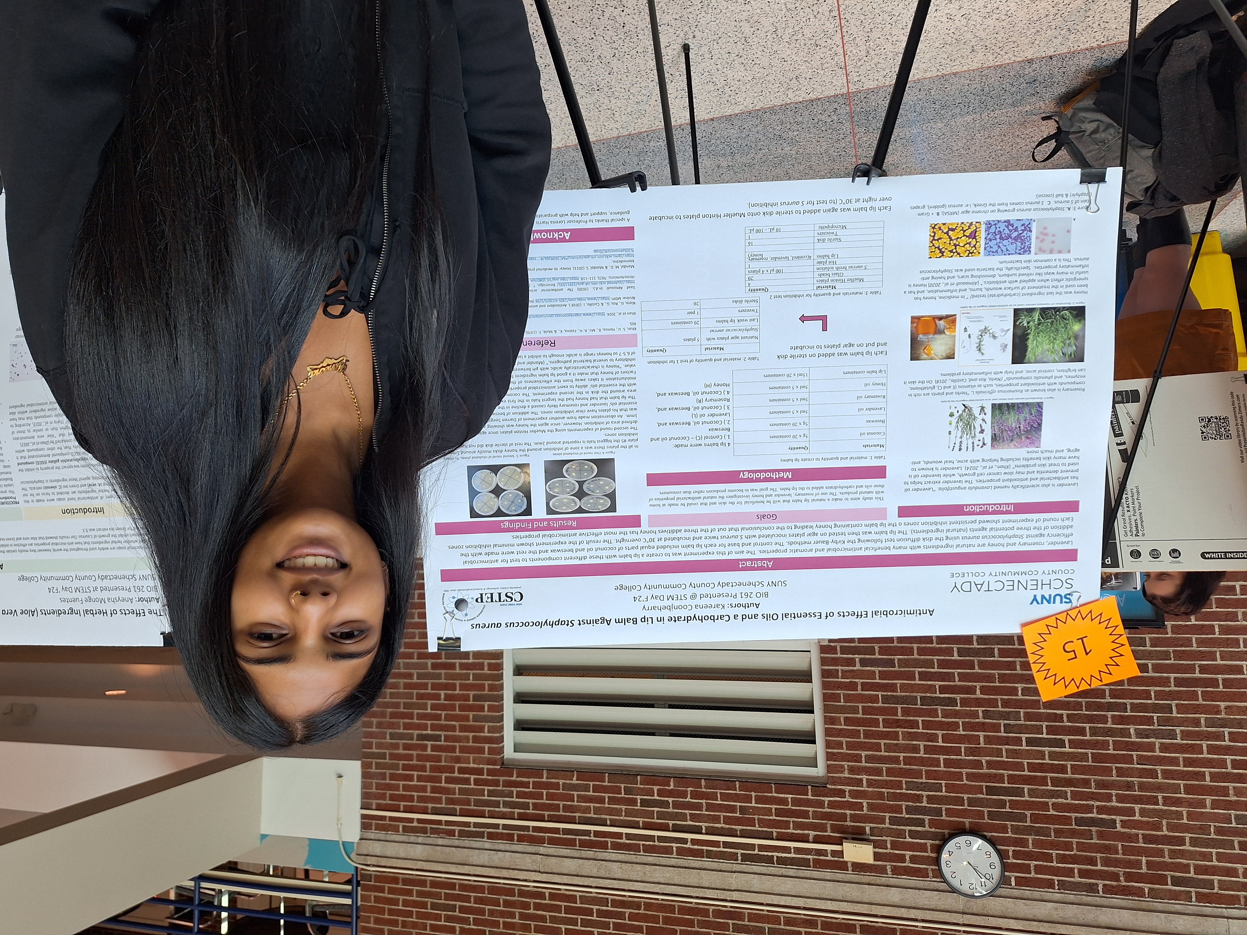 Science student smiling, standing in front of research poster on easel