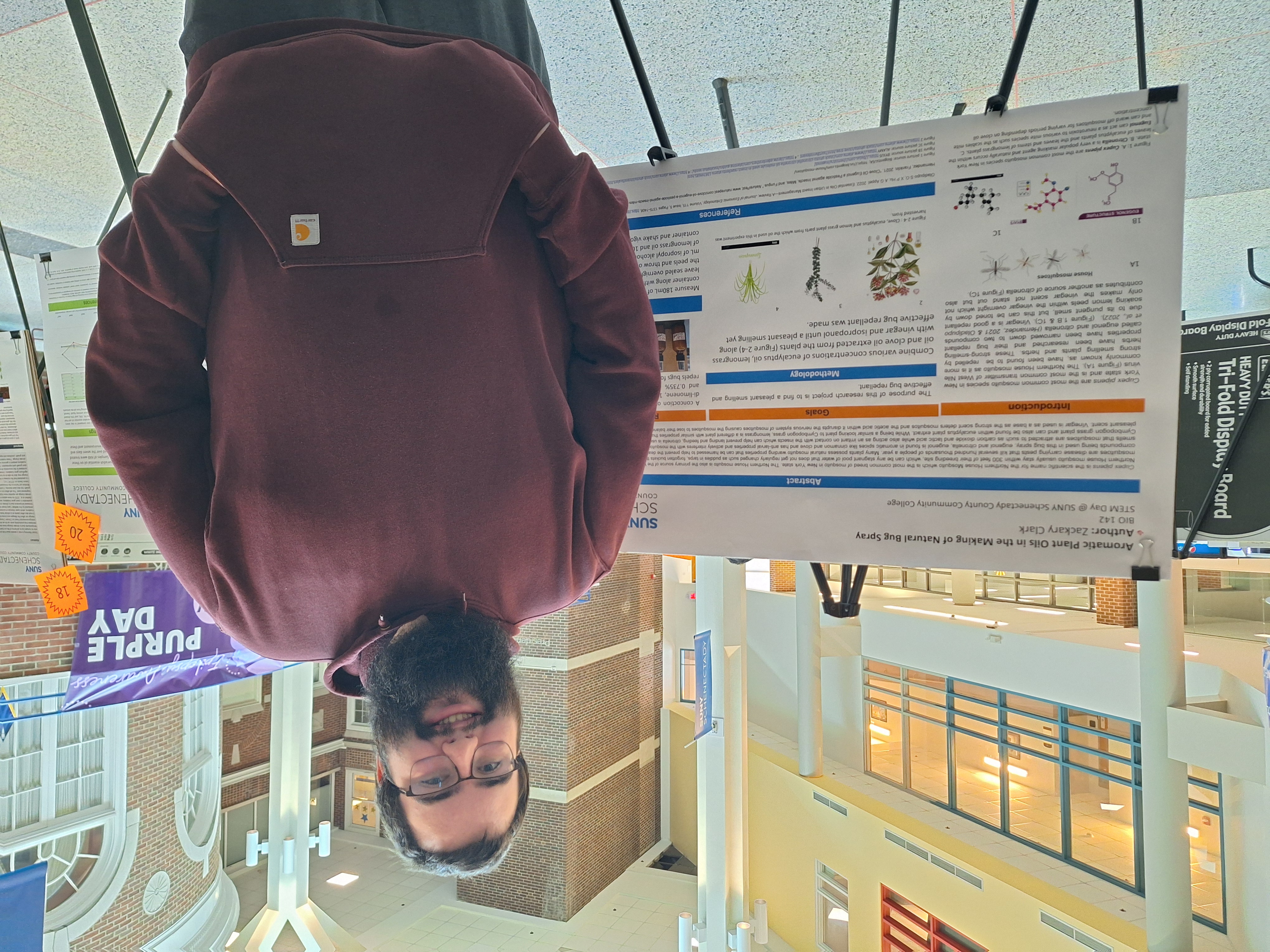 Science student smiling, standing in front of research poster on easel