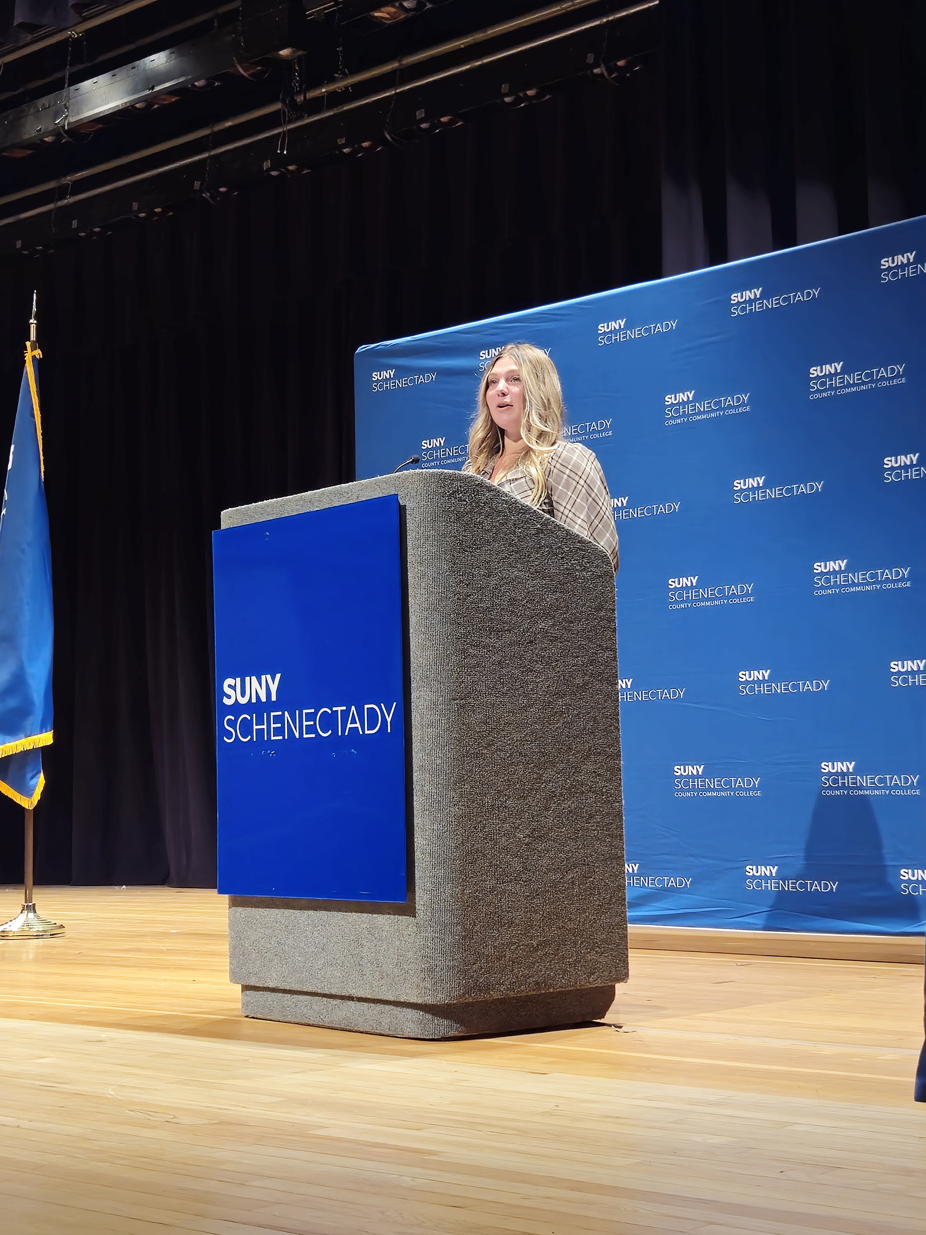 Alexa Angel standing at podium on stage, speaking