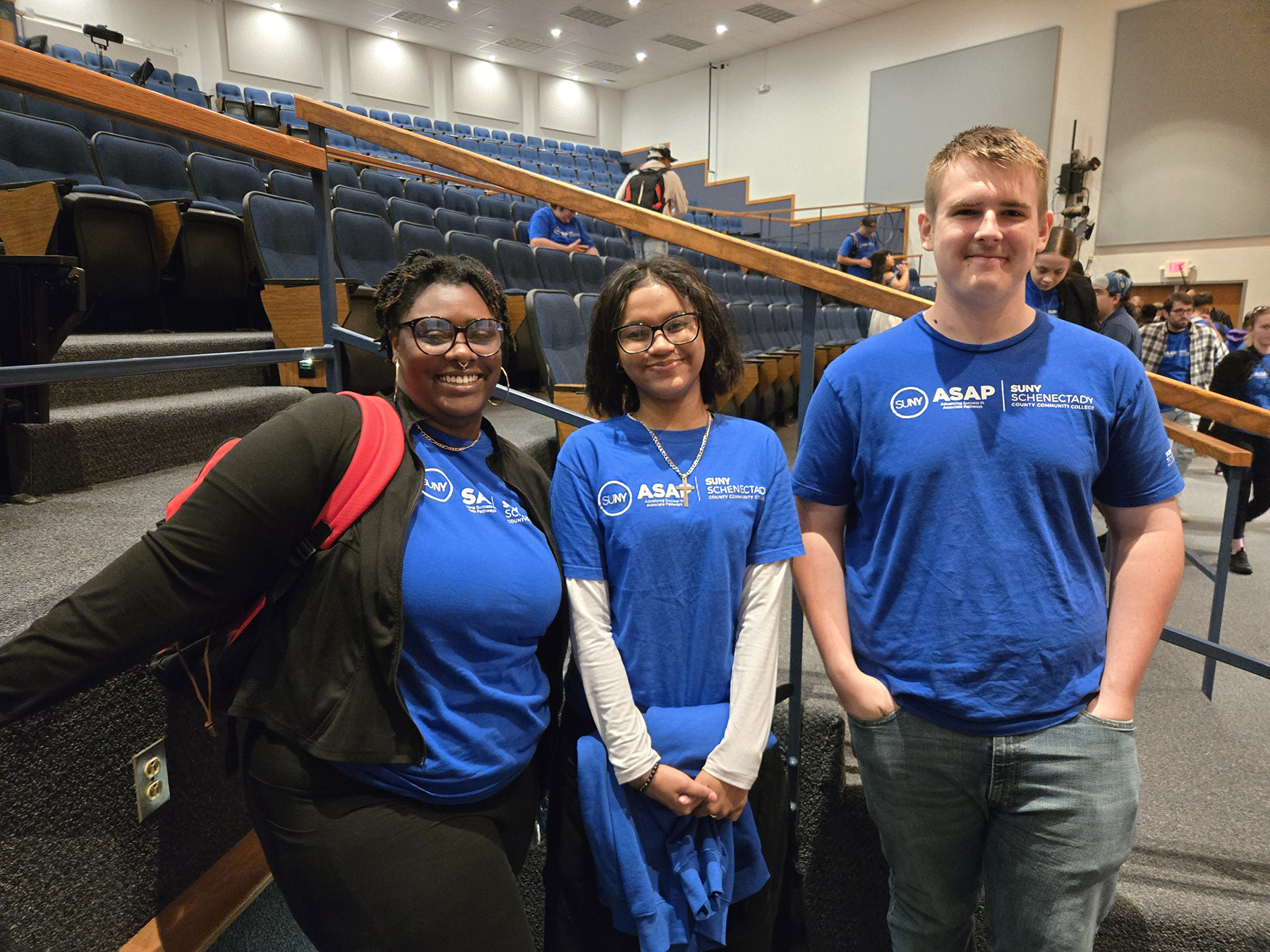 Three students, wearing blue ASAP tshirt, standing inside auditorium