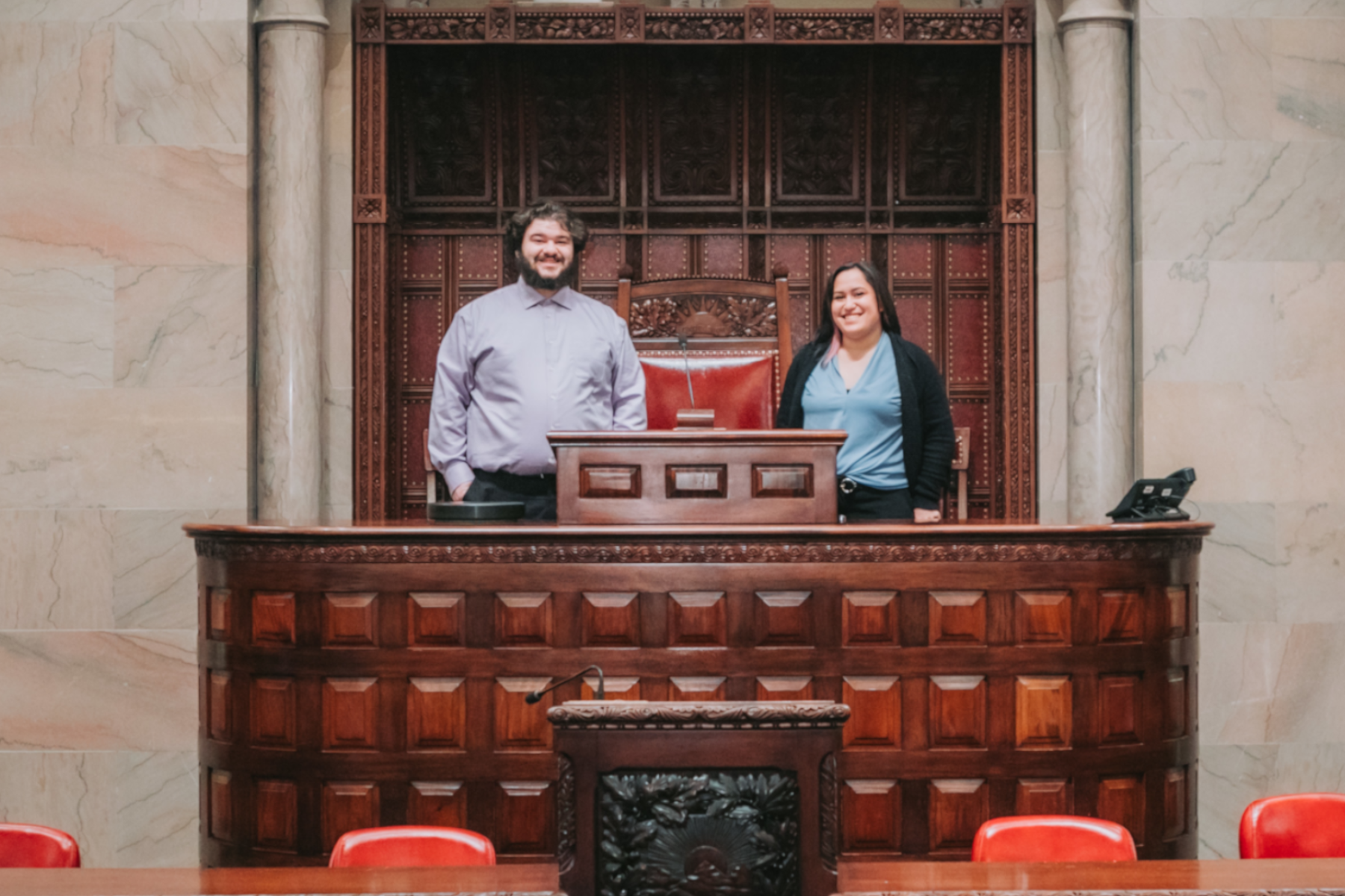 Student interns Nate Friedman and Rayanne Vasquez standing on the floor of the NYS Senate