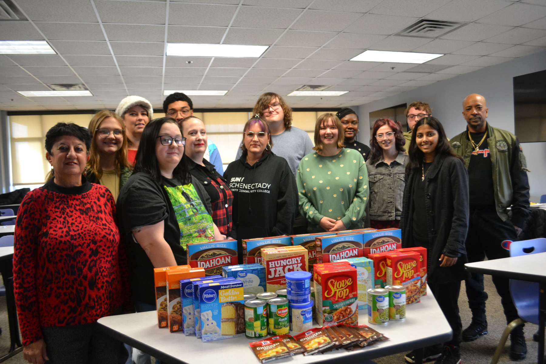 Students and Professor Adamany in Sociology class standing in front of table that has food items stacked on it