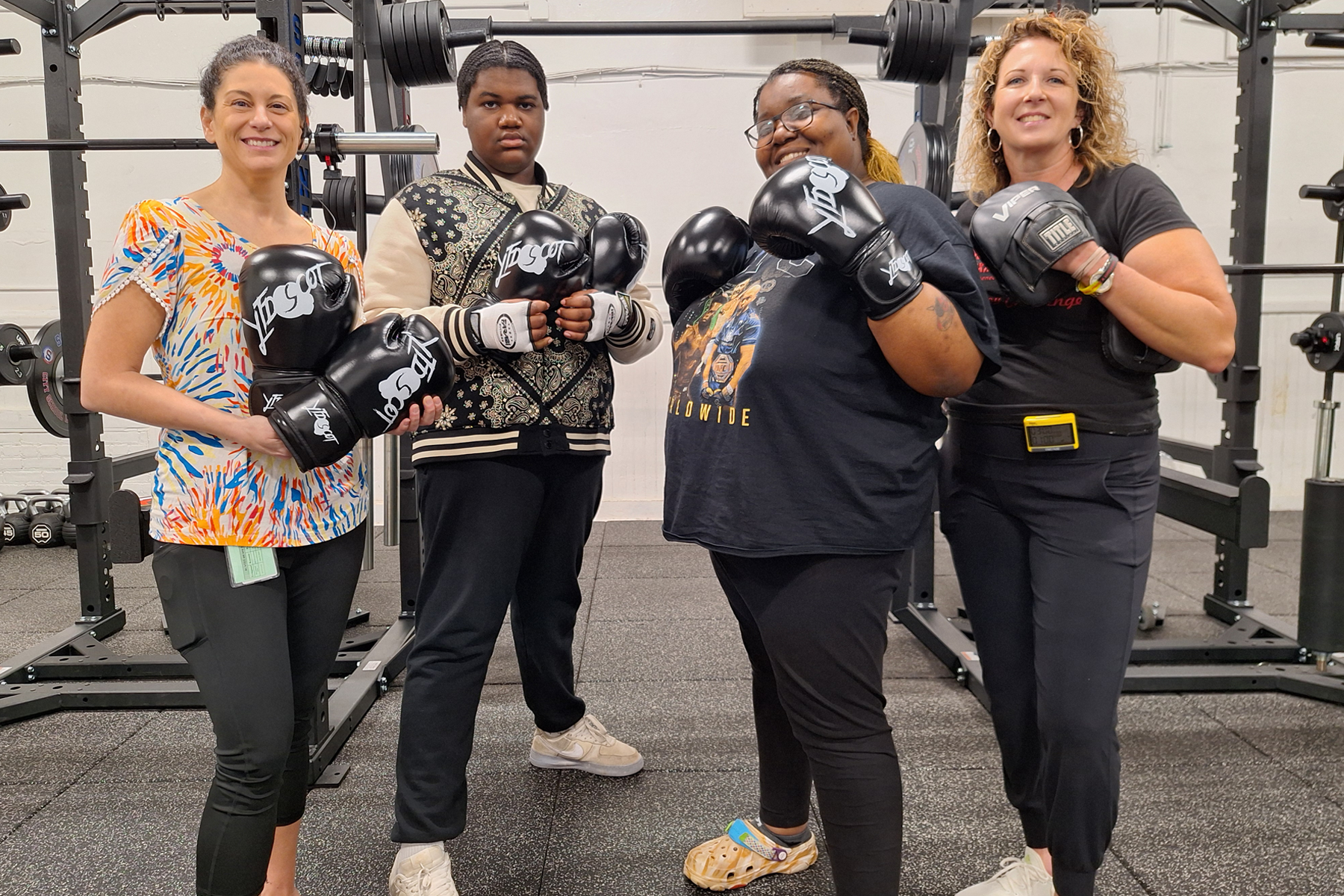 School official, students, and boxing director wearing boxing gloves, standing in gym.