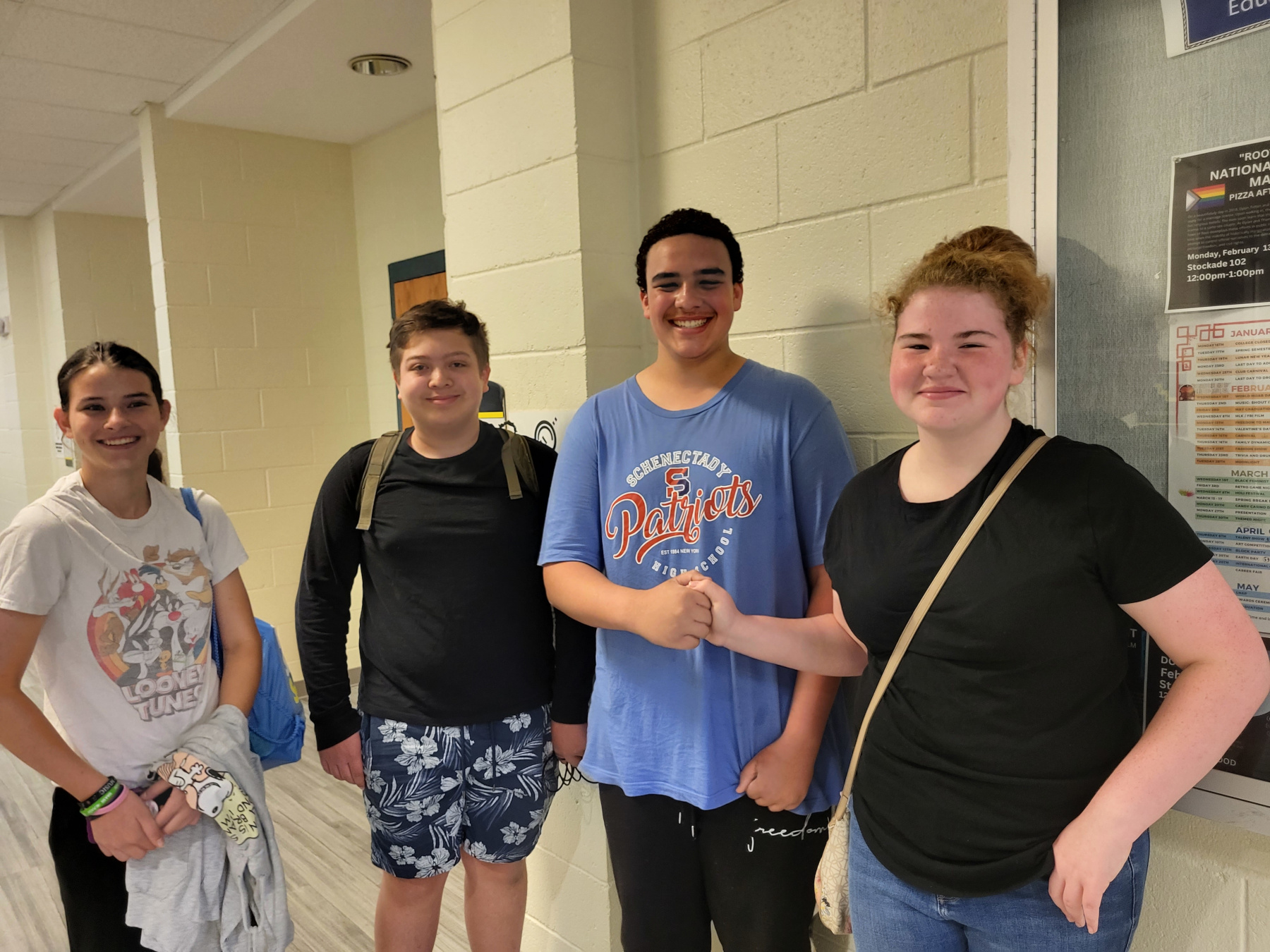 Four students, smiling, standing in hallway