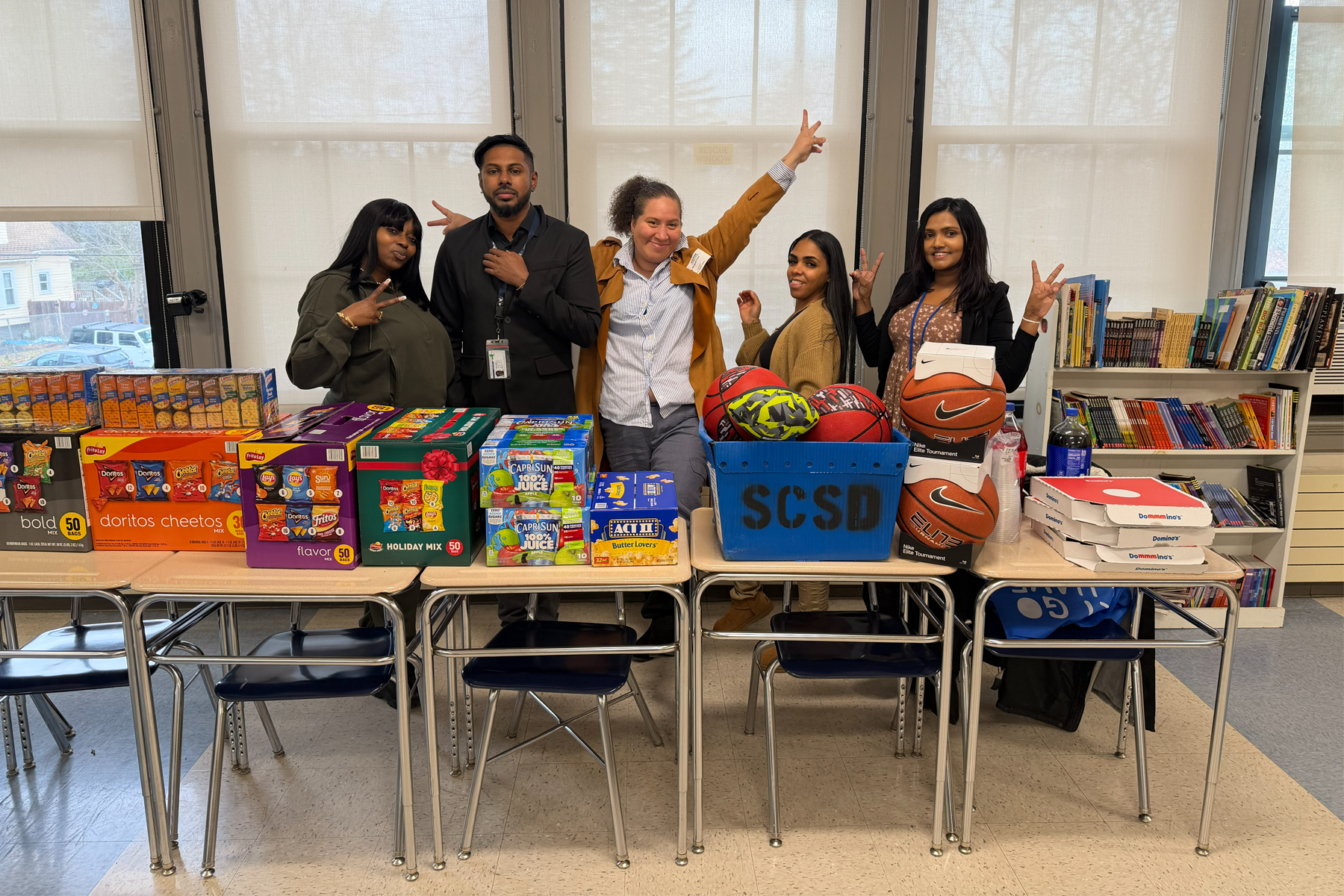 Students standing behind table that is stacked with items they collected and are donating