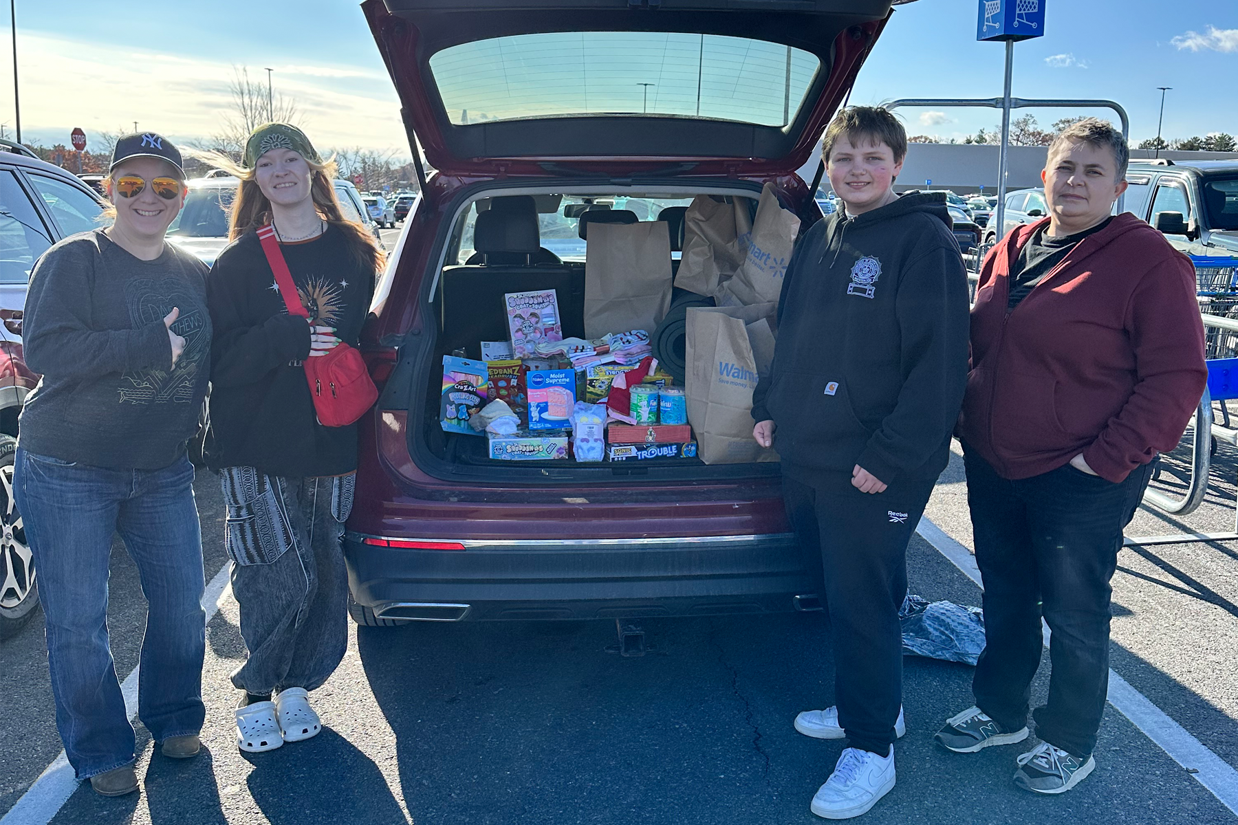 Students standing near car with trunk open to show items they are donating