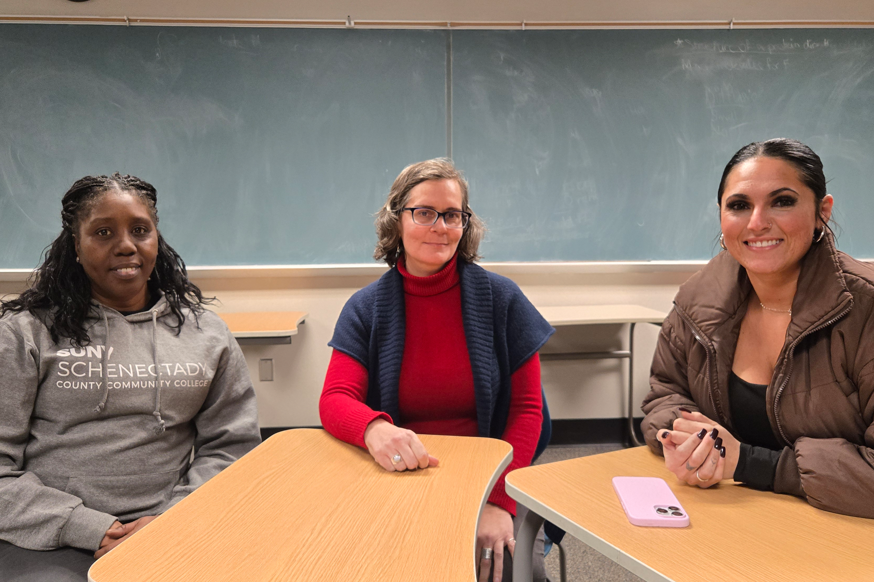 Three students, sitting at desks, smiling