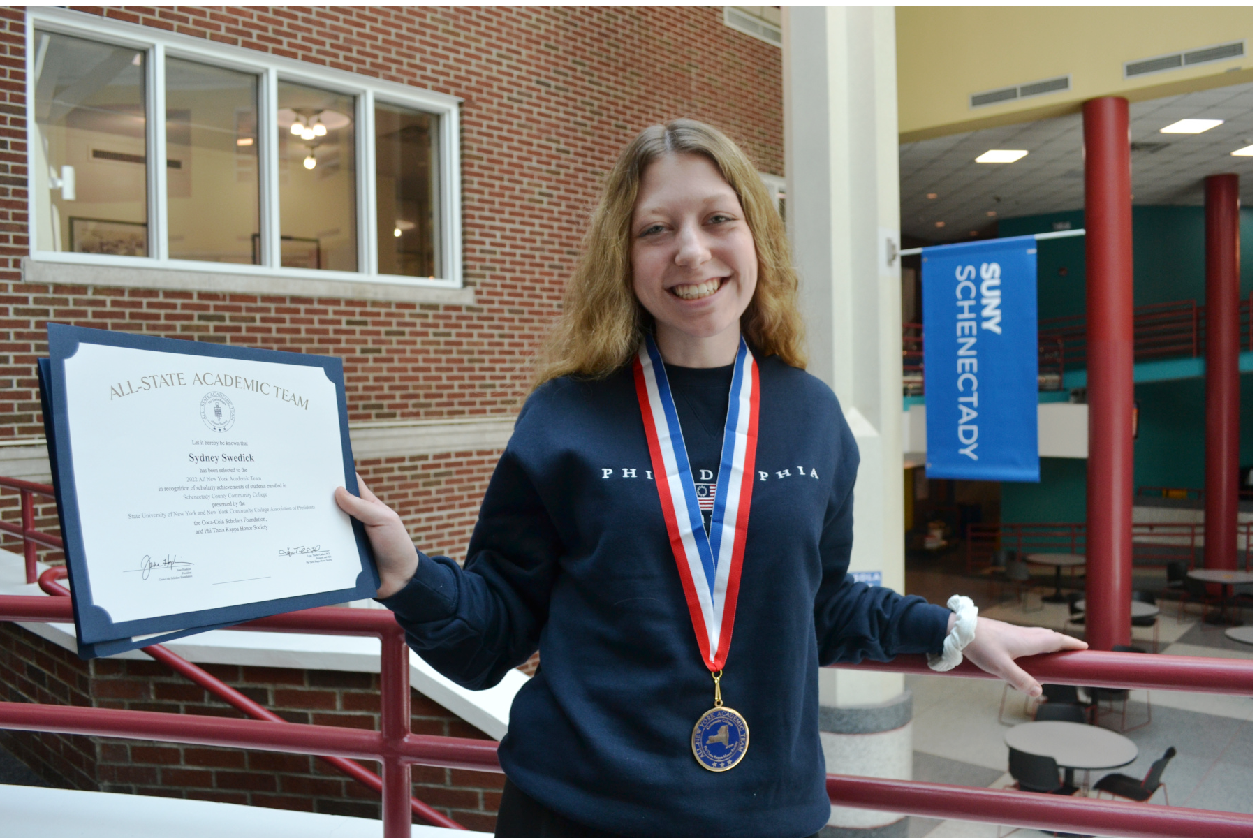 Sydney Swedick holding All-New York Team certificate standing in Elston Hall