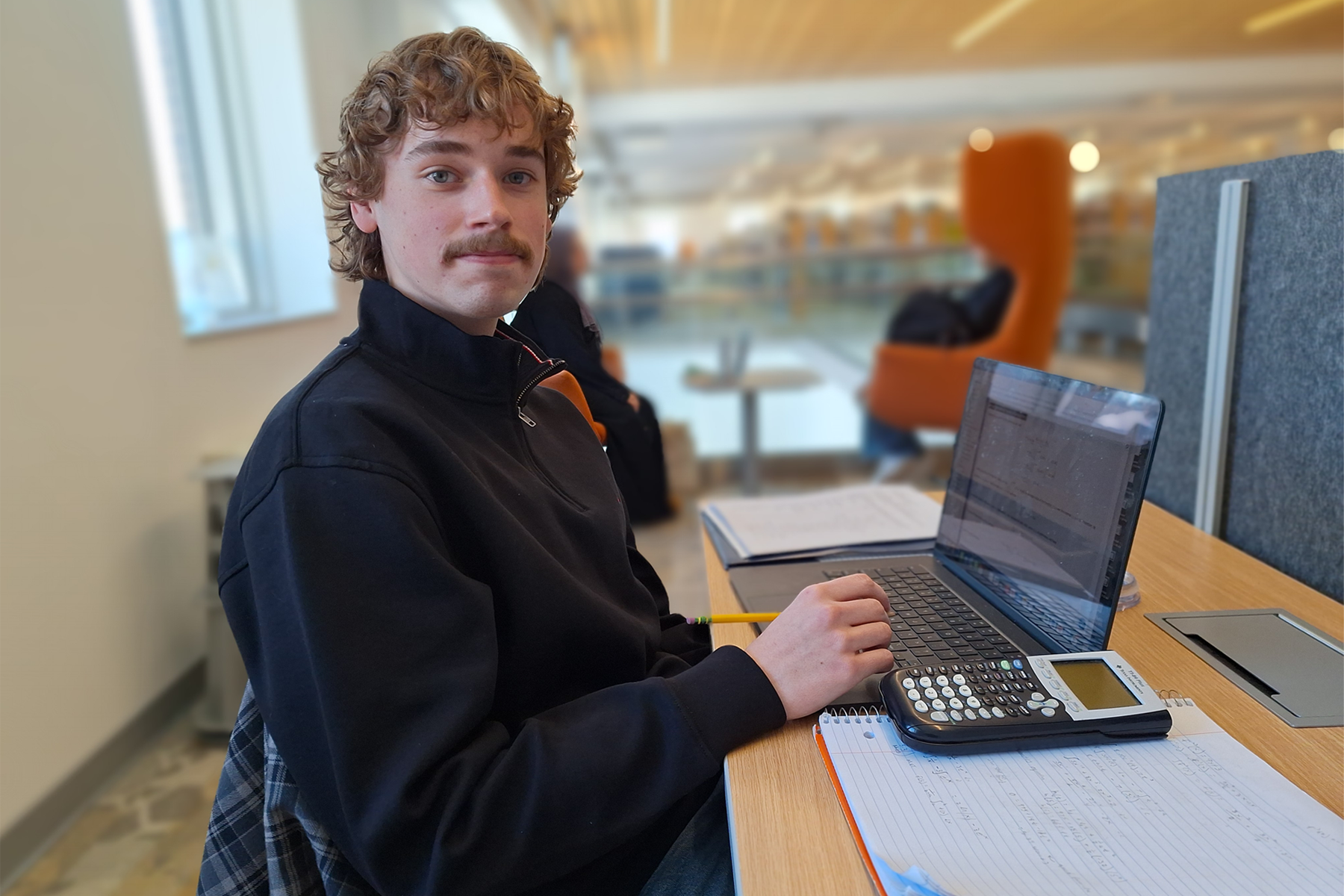 Tanner Litts, sitting at desk in Library with laptop and calculator, smiling