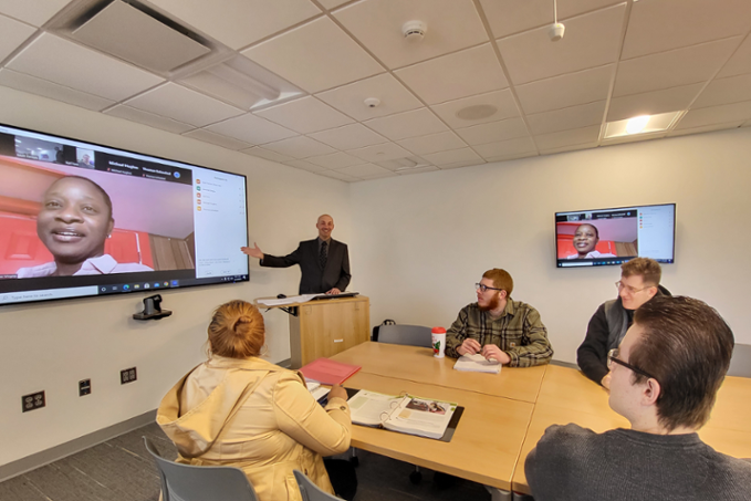 Professor Matt Farron with students in classroom and on screen at front of the room