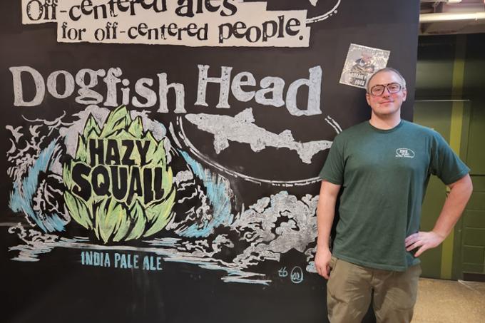 James Hanley standing in front of Dogfish Head Craft Brewery sign