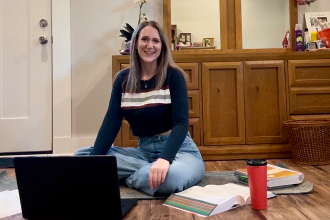 Student Meghan Conley with her laptop and books sitting on floor 