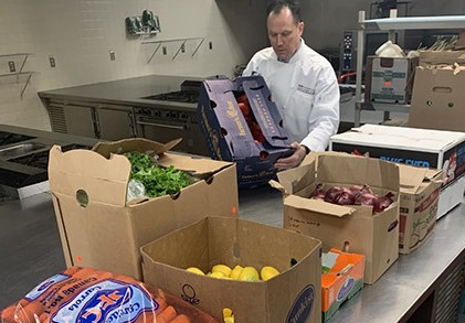 Dr. Dave Brough loading food donations. Boxes of lemons, limes, and lettuce, along with bags of carrots in the foreground.