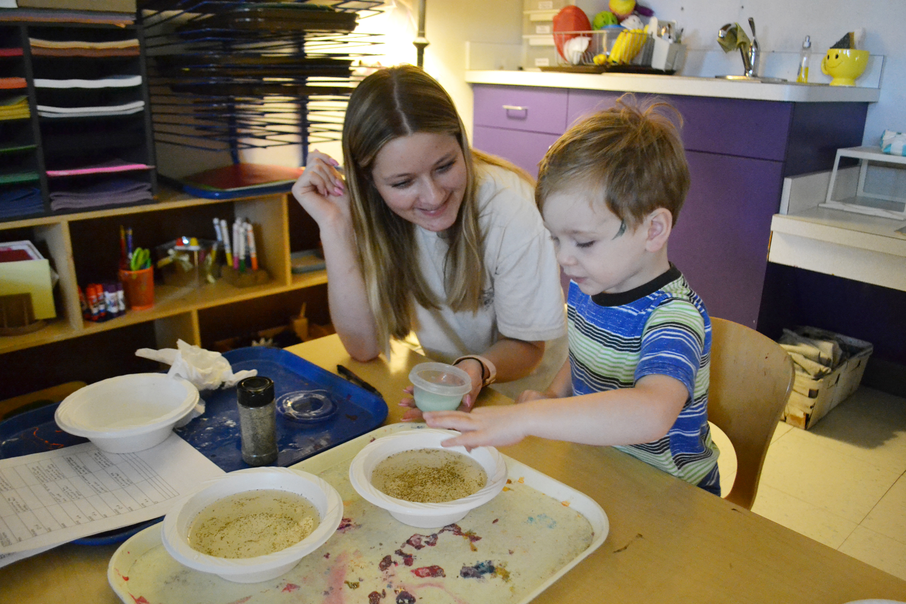 College student and child doing art activity at table in preschool