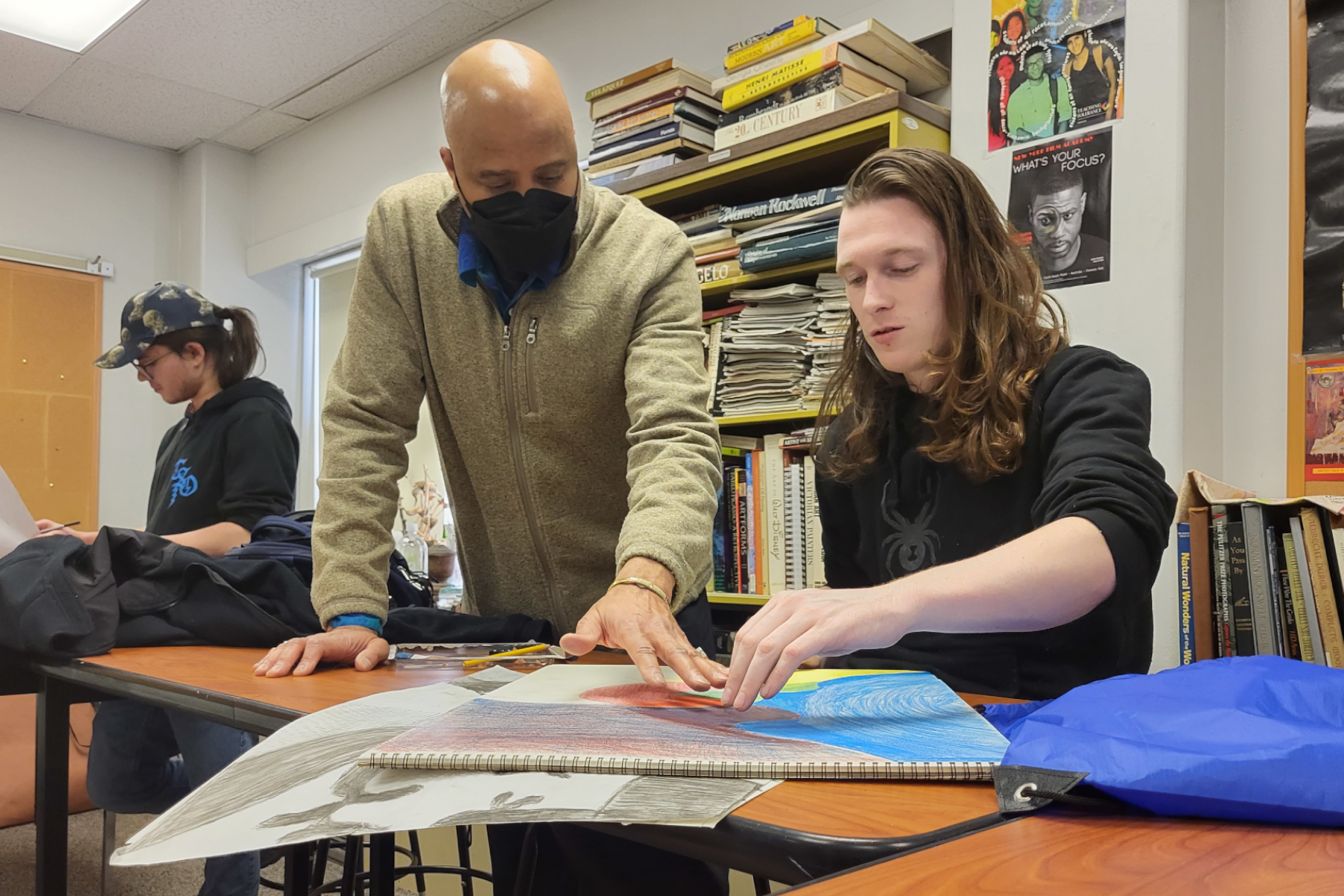 Stephen Tyson speaking with a student at art table as student works on a drawing
