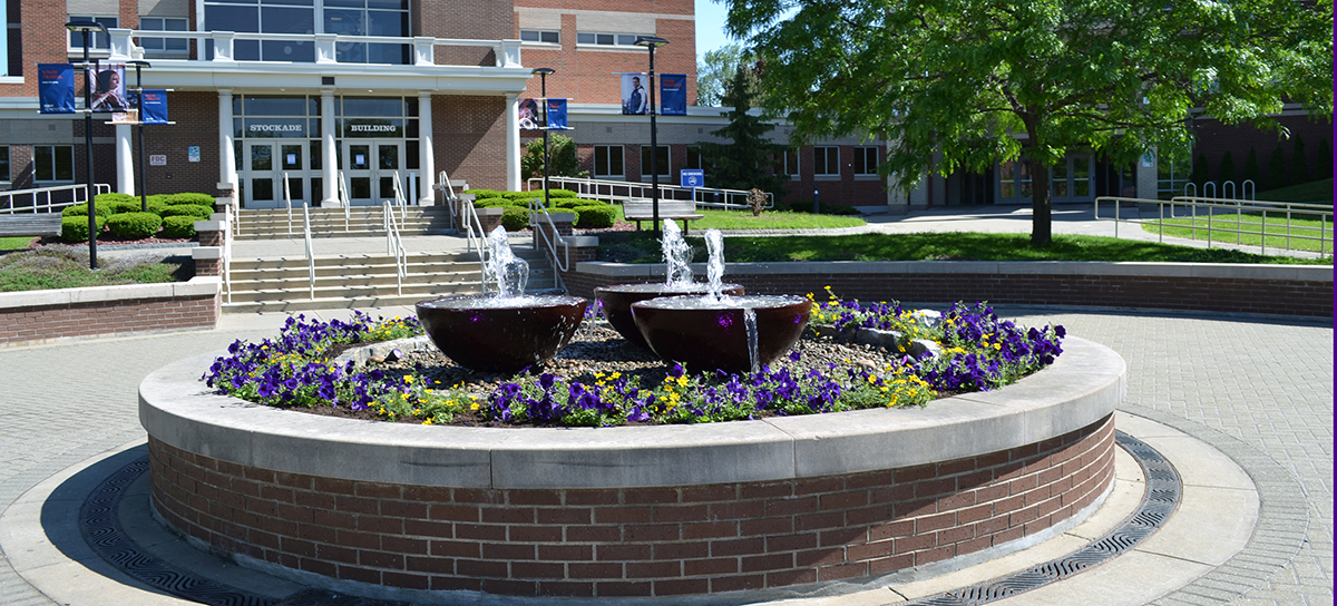 Fountain in the center of the Quad at SUNY Schenectady, flowers growing around it.